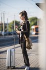 Молода жінка з багажем на трамвайній станції в місті за допомогою мобільного телефону — стокове фото
