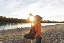 Sportliche Frau macht Pause am Fluss, trinkt Wasser — Stockfoto