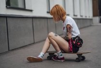 Jeune femme assise sur le skateboard sculpteur sur le trottoir — Photo de stock