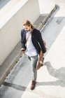 Jeune homme d'affaires portant skateboard, en utilisant un smartphone — Photo de stock
