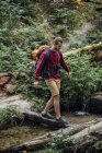 Giovane escursionista con zaino che attraversa l'acqua nella foresta — Foto stock