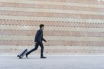 Ejecutando joven hombre de negocios con la maleta rodante - foto de stock