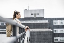 Joven empresaria sosteniendo teléfono inteligente y apoyándose en el puente - foto de stock