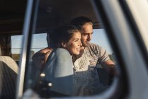 Любящая пара, сидящая в своем фургоне с руками вокруг, наблюдая закат — стоковое фото