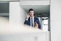 Businessman with briefcase walking in office building, using smartphone — Stock Photo