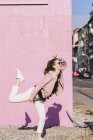 Mujer joven y feliz moviéndose frente a la pared rosa - foto de stock