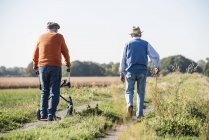 Vecchi amici fare una passeggiata nei campi con bastone da passeggio e camminatore a ruote, parlando dei vecchi tempi — Foto stock