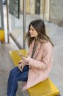 Jeune femme avec téléphone portable en attente à l'arrêt de bus — Photo de stock