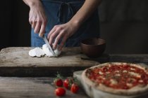 Молодий чоловік готує піцу, розрізаючи моцарелу на дошці — стокове фото