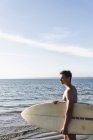 Франция, Бриттания, молодой человек с доской для серфинга, стоящий в море — стоковое фото