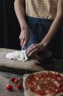 Молодий чоловік готує піцу, розрізаючи моцарелу на дошці — стокове фото