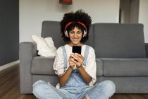Smiling woman sitting at home with headphones and cell phone — Stock Photo