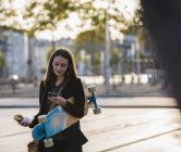 Jovem com longboard e lanche na cidade verificando celular — Fotografia de Stock