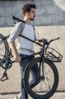 Joven llevando bicicleta fija de cercanías en la pared de hormigón - foto de stock