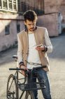 Молодой человек с пригородным велосипедом на заднем дворе в городе проверяет сотовый телефон — стоковое фото