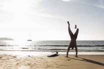 France, Bretagne, jeune homme faisant un handstand sur la plage près de la planche de surf — Photo de stock