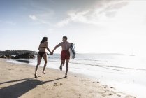 Francia, Bretaña, pareja joven con tabla de surf en la mano en el mar - foto de stock