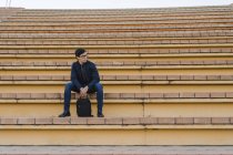 Jeune homme d'affaires avec sac à dos assis sur les escaliers regardant la distance — Photo de stock