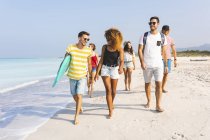 Group of friends walking on the beach, carrying surfboard — Stock Photo