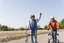 Two old friends wearing safety helmets, competing in a wheeled walker race  — Senior Men, success - Stock Photo | #283103294