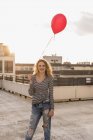 Portrait of young woman with red balloon on roof terrace at sunset — Stock Photo