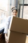Retrato de jovem sorridente carregando caixas de papelão em novo apartamento na janela — Fotografia de Stock