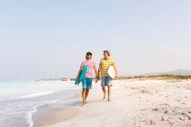 Amigos andando na praia, carregando pranchas de surf — Fotografia de Stock