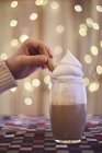 Hand and coffee with cream, bokeh lights on the background — Stock Photo