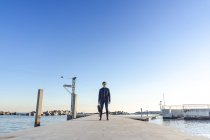 Young businessman with backpack standing on jetty — Stock Photo