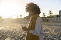 Donna con sciarpa gialla, con smartphone sulla spiaggia — Foto stock