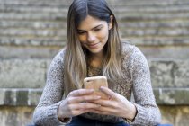 Молодая женщина сидит на лестнице на улице с помощью мобильного телефона — стоковое фото