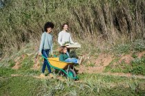 Famiglia che cammina su una pista sterrata, spingendo carriola, portando cassa con verdure — Foto stock