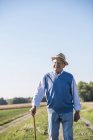 Senior man with a walking stick, walking in the fields — Stock Photo