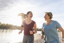 Granddaughter and grandmother having fun, jogging together at the river — Stock Photo