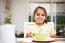 Portrait d'une petite fille souriante prenant le petit déjeuner à la maison — Photo de stock