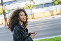 Portrait of smiling young woman listening music with earphones and smartphone — Stock Photo