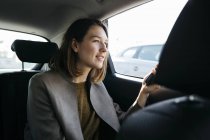 Smiling woman sitting in back seat of a car holding cell phone — Stock Photo
