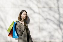 Portrait of smiling woman with shopping bags standing at a wall — стокове фото