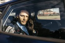 Человек, сидящий на заднем сидении машины и разговаривающий по мобильному телефону — стоковое фото
