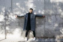 Rindo jovem vestindo pulôver gola alta e casaco cinza em pé na frente da parede de concreto — Fotografia de Stock