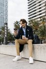Испания, Барселона, человек, сидящий в городе с кофе и мобильным телефоном — стоковое фото