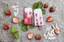 Homemade strawberry coconut ice lollies with fresh strawberries and coconut slices on granite — Stock Photo