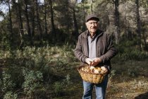 Retrato de un hombre mayor sonriente sosteniendo la cesta llena de setas en el bosque - foto de stock