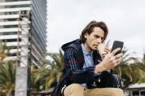Espagne, Barcelone, homme sérieux assis dans la ville avec café à emporter et téléphone portable — Photo de stock