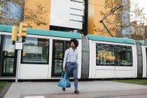 Spain, Barcelona, man with bag crossing the street in front of a tramway — Stock Photo