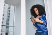Portrait of smiling young woman using smartphone and earphones at home — Stock Photo