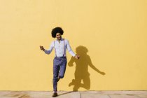 Улыбающийся мужчина танцует перед желтой стеной — стоковое фото