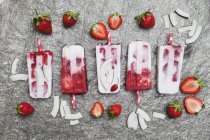Homemade strawberry coconut ice lollies with fresh strawberries and coconut slices on granite — Stock Photo