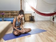 Smiling young woman sitting on yoga mat looking at cell phone — Stock Photo