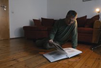 Senior man sitting on the floor at home looking at photo album — Stock Photo